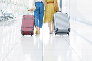 Duas pessoas caminhando lado a lado em um aeroporto, cada uma puxando sua bagagem de mão sobre o piso brilhante do terminal.