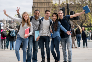 Grupo de cinco jovens sorrindo ao ar livre com cadernos nas mãos, representando a experiência de intercâmbio para adolescentes no exterior.