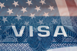 Imagem de um visto americano com parte da bandeira dos Estados Unidos ao fundo.